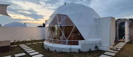 A geodesic dome structure with a glass window, surrounded by a white wall and a pathway.