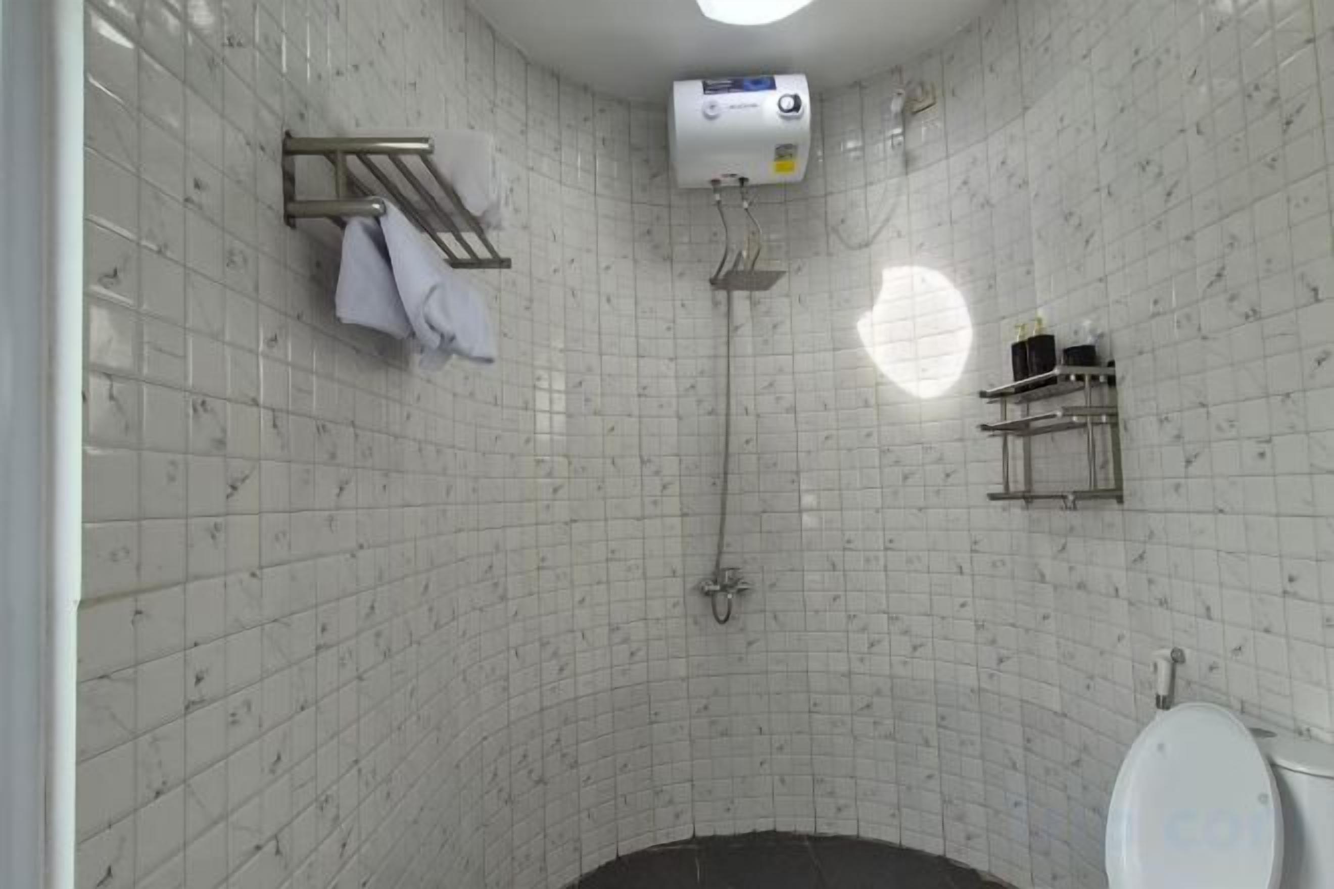 A bathroom with white tiled walls, a shower, a toilet, and a towel rack.