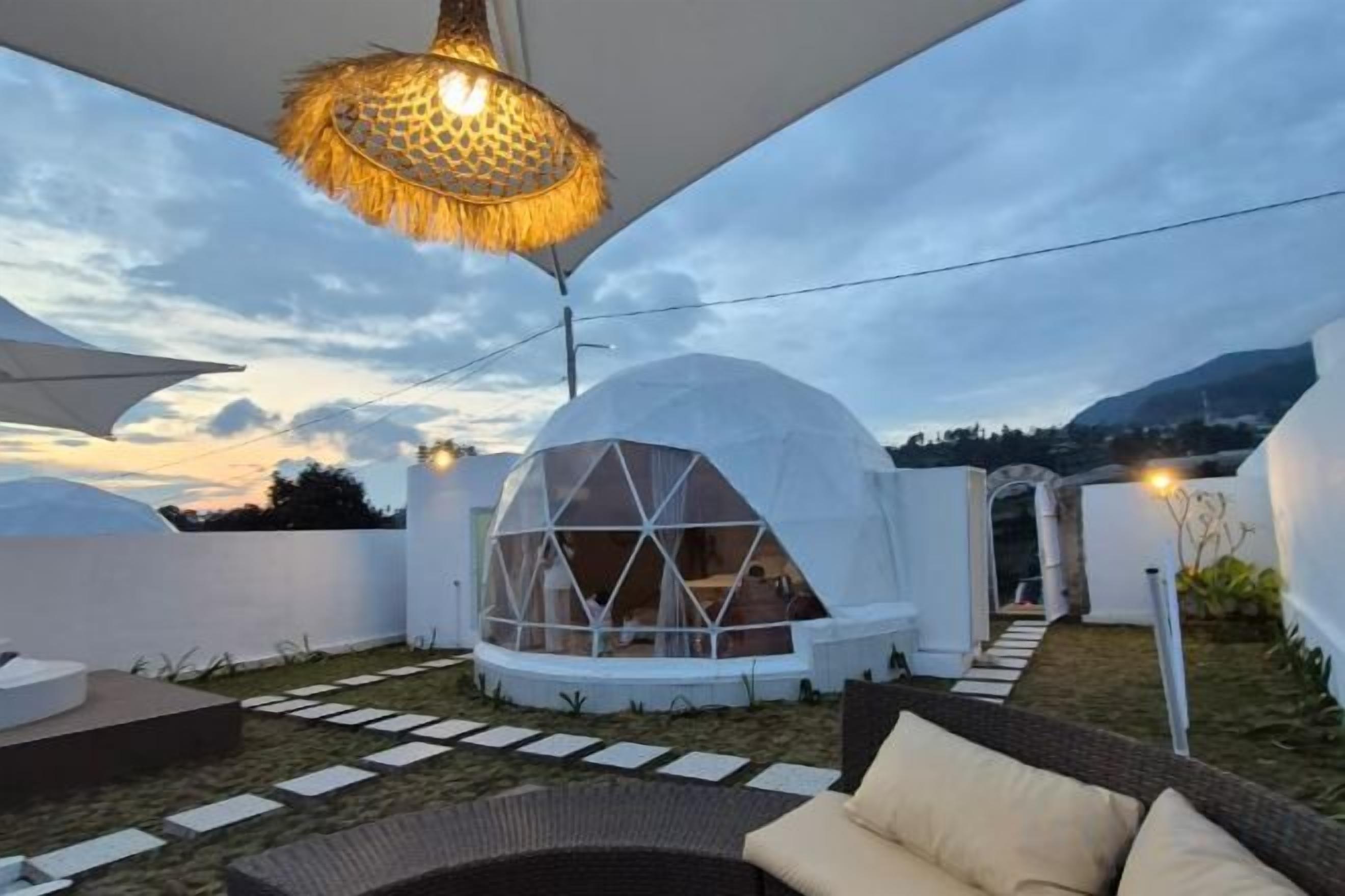 A modern outdoor seating area with a dome-shaped structure, a hanging light fixture, and a pathway leading to a covered entrance.