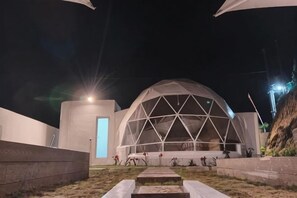 Een modern gebouw met een koepelstructuur, een pad naar de ingang en een klein tuintje.