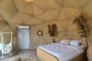 Een tentvormige kamer met een bed, hangstoel en een wandairconditioner.