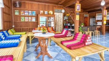 A room with a wooden ceiling, a large window, a sofa set, a dining table, and a staircase.