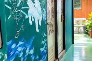 A hallway with a mural, a wooden door, and a view of an outdoor area with a table and chairs. - Baanpai Hostel (Pai)