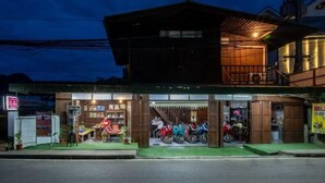 A building with a wooden facade, a covered entrance, and a motorcycle parking area. - Baanpai Hostel (Pai)