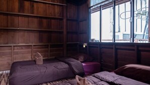 A room with wooden paneling, a window with metal bars, and a bed with a purple mattress. - Baanpai Hostel (Pai)