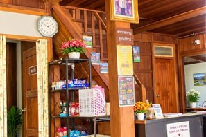 A reception area with a wooden interior, a clock, a flower arrangement, and a sign indicating check-out times. - Baanpai Hostel (Pai)