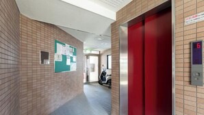 Un couloir avec un ascenseur rouge, un écran numérique affichant le chiffre 6, et un scooter garé au loin.