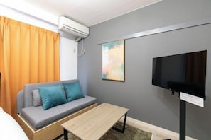 A hotel room with a gray sofa, a wooden table, a TV on a stand, and an air conditioning unit. - Collection Yuunagi (Osaka)