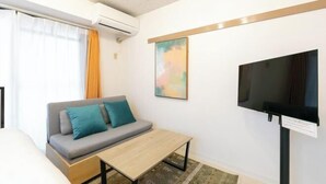 Une chambre d’hôtel équipée d’un canapé, d’une petite table, d’un téléviseur à écran plat fixé au mur et d’un appareil de climatisation.