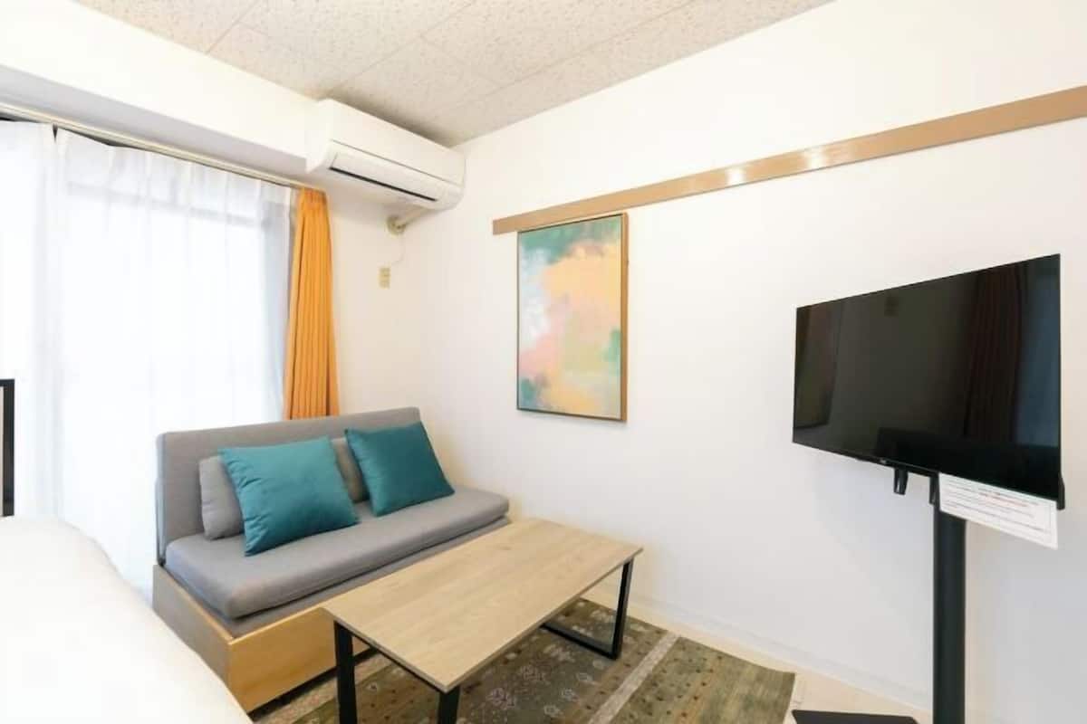 Ein Hotelzimmer mit Sofa, kleinem Tisch, flachbildfernseher an der Wand und Klimaanlage.