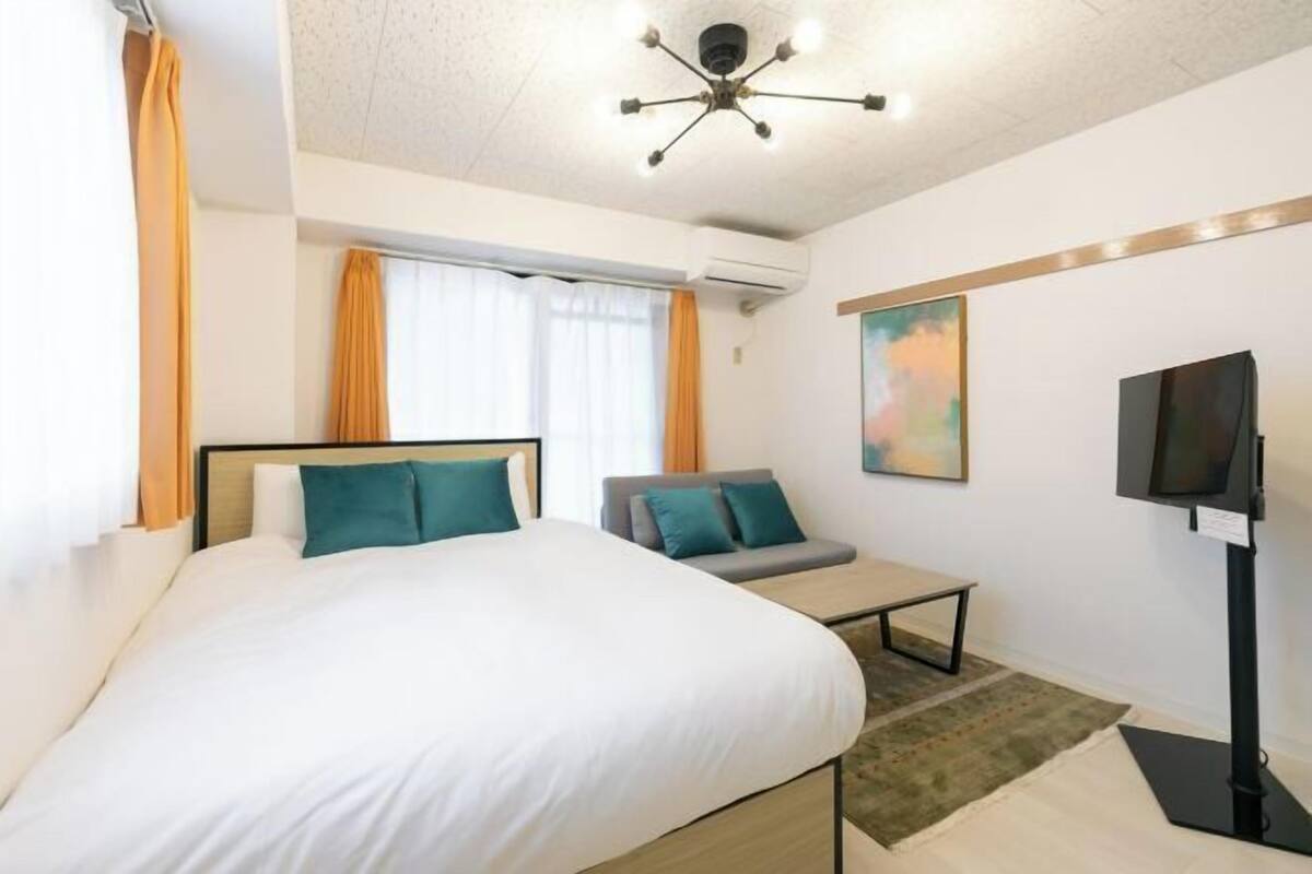 A hotel room with a bed, a sofa, a TV, and a painting on the wall.