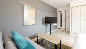 Un salon moderne avec un canapé gris, des coussins turquoise, une table basse en bois, un téléviseur à écran plat et une armoire.
