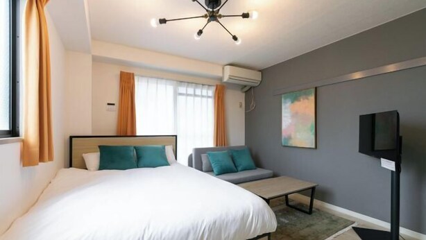 Une chambre d’hôtel moderne avec un grand lit, un petit canapé, une télévision et un luminaire fixé au plafond.