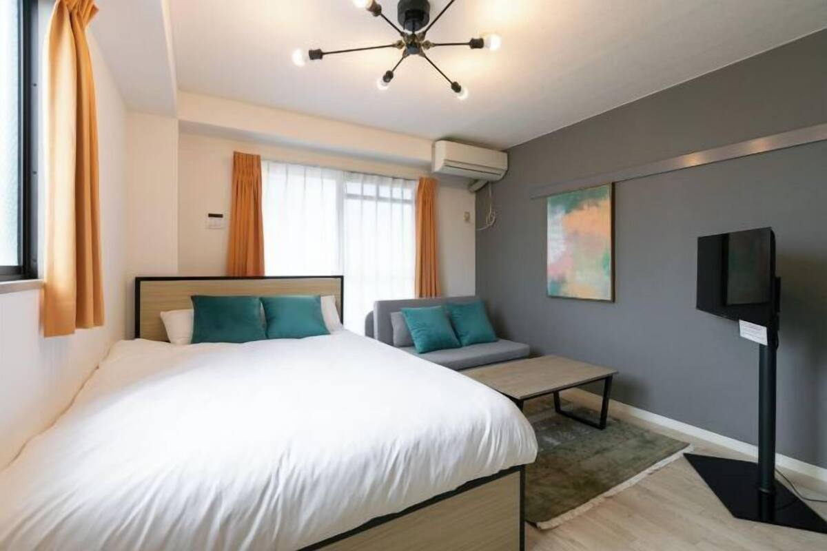 Ein modernes Hotelzimmer mit einem großen Bett, einer kleinen Couch, einem Fernseher und einer Deckenleuchte.