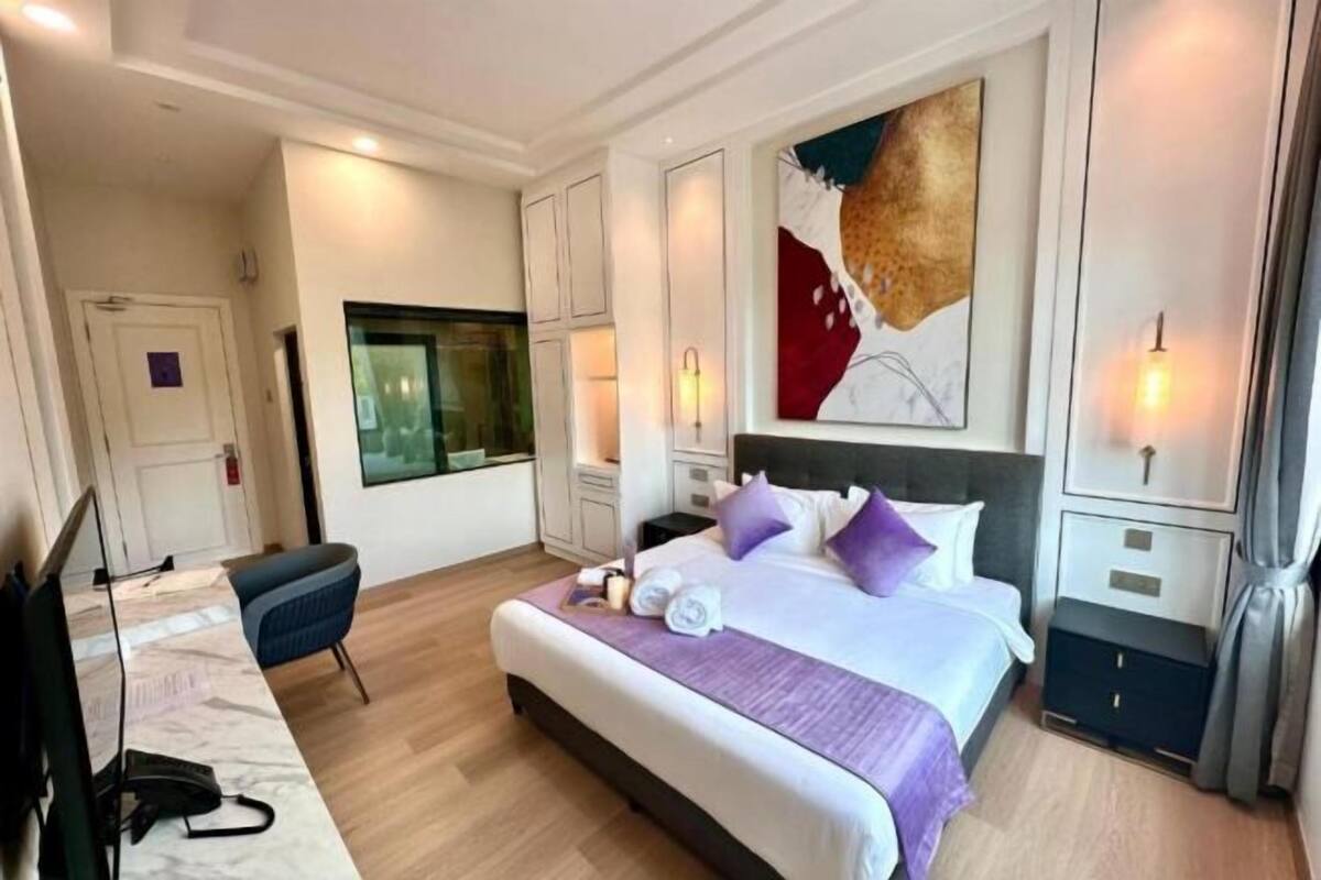 A hotel room with a bed, a desk, a chair, a TV, and a large abstract painting on the wall.