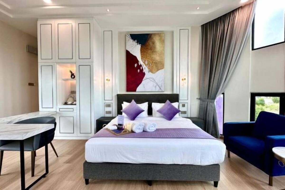 A modern hotel room with a large bed, a desk, a chair, and a painting on the wall.