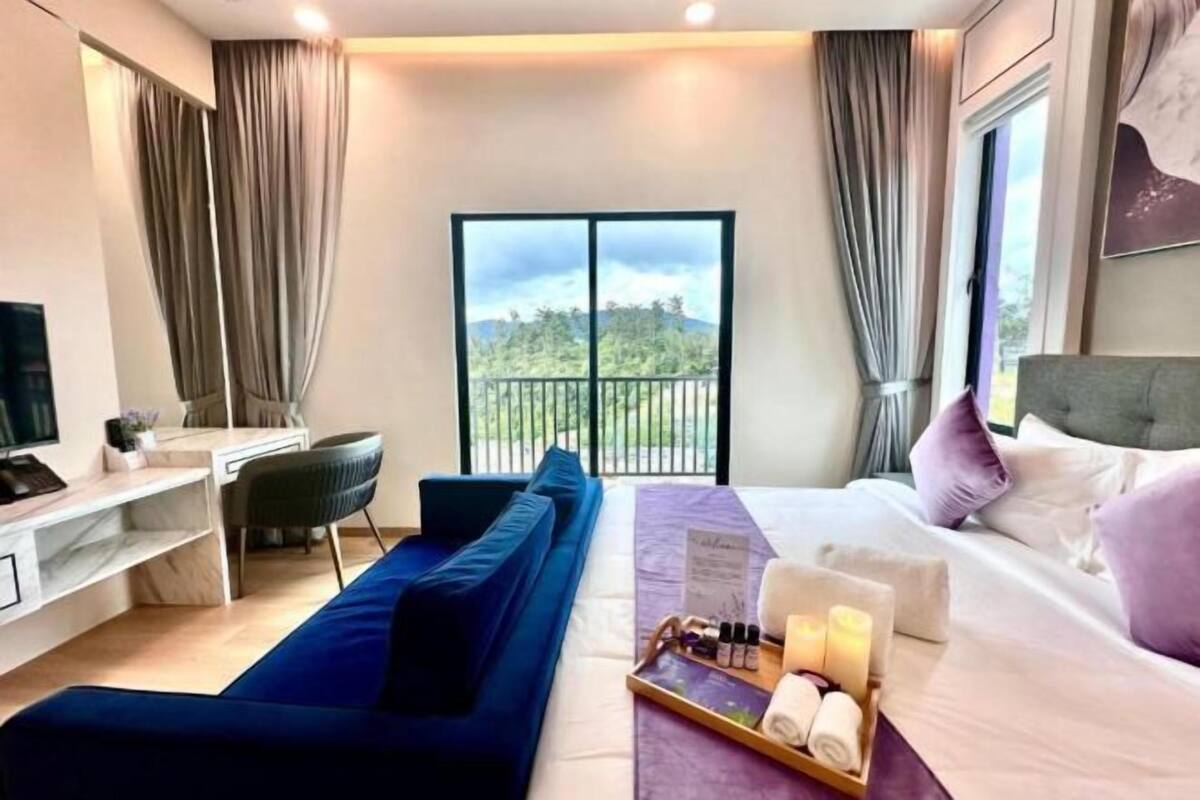 A hotel room with a bed, a desk, a sofa, and a balcony with a view.
