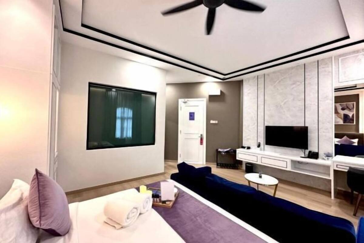 A modern hotel room with a bed, a sofa, a desk, a TV, and a ceiling fan.
