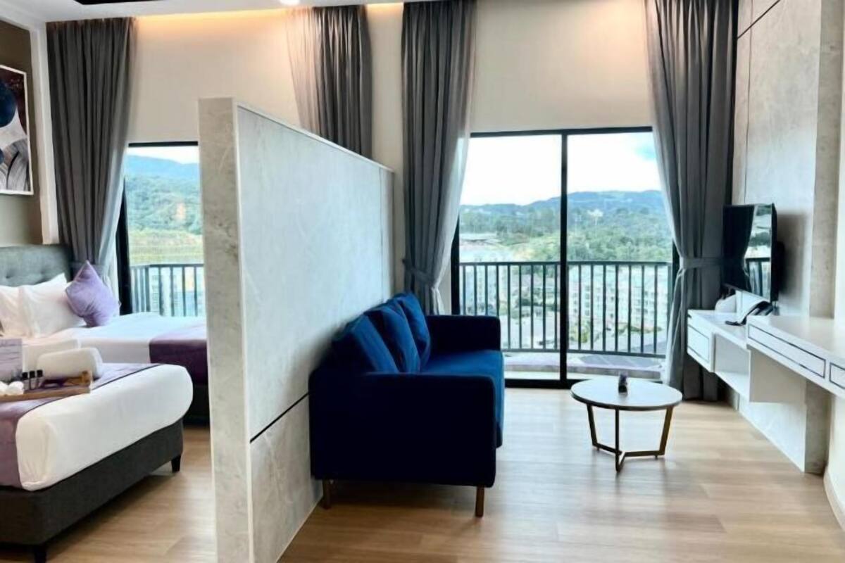 A modern hotel room with a bed, sofa, small table, and a balcony with a view.