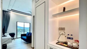 A modern hotel room with a balcony, a sofa, a kitchen area with a kettle and tea set, and a shelf with bottled water and tea bags. - Cameron Lavender Mansion (Brinchang)