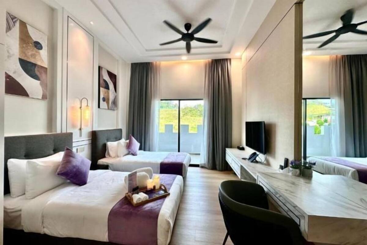 A hotel room with two beds, a desk, a chair, a ceiling fan, and a large window with curtains.