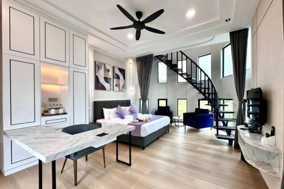 A modern hotel room with a bed, a desk, a chair, a staircase, and a ceiling fan.