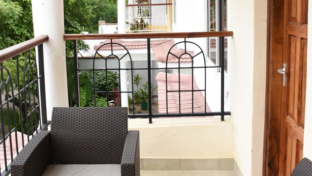 A balcony with wicker furniture, a wooden door, and a view of a building with a red roof. - Tremendous 4-bedroom bungalow in Kilifi County (Kilifi County)