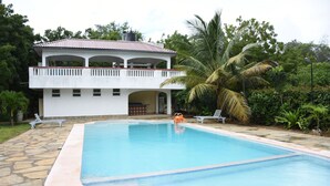 A swimming pool with a stone border, a white building with a balcony, and a palm tree. - Tremendous 4-bedroom bungalow in Kilifi County (Kilifi County)