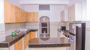 A kitchen with wooden cabinets, a marble countertop, a stainless steel refrigerator, and a microwave. - Tremendous 4-bedroom bungalow in Kilifi County (Kilifi County)