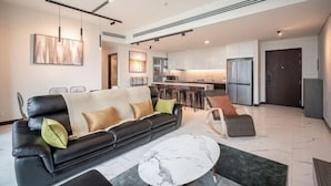 A modern living room with a black leather sofa, a marble coffee table, and a kitchen in the background. - The Metropole Riverside Apartment (Ho Chi Minh City)