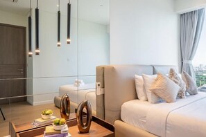 A modern hotel room with a large bed, a bedside table with books and a plant, and a view through a glass wall. - The Metropole Riverside Apartment (Ho Chi Minh City)