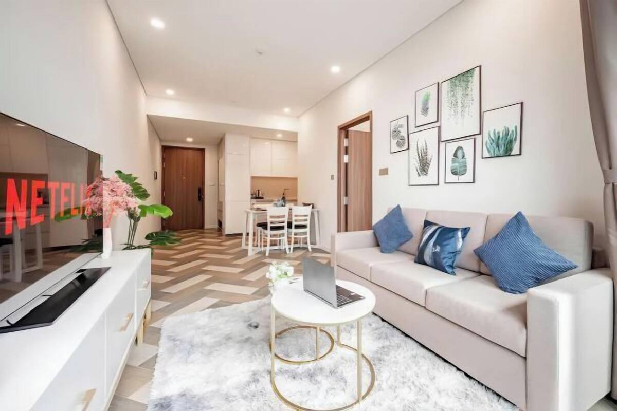 A modern living room with a sofa, a coffee table, a TV, and a dining area in the background.