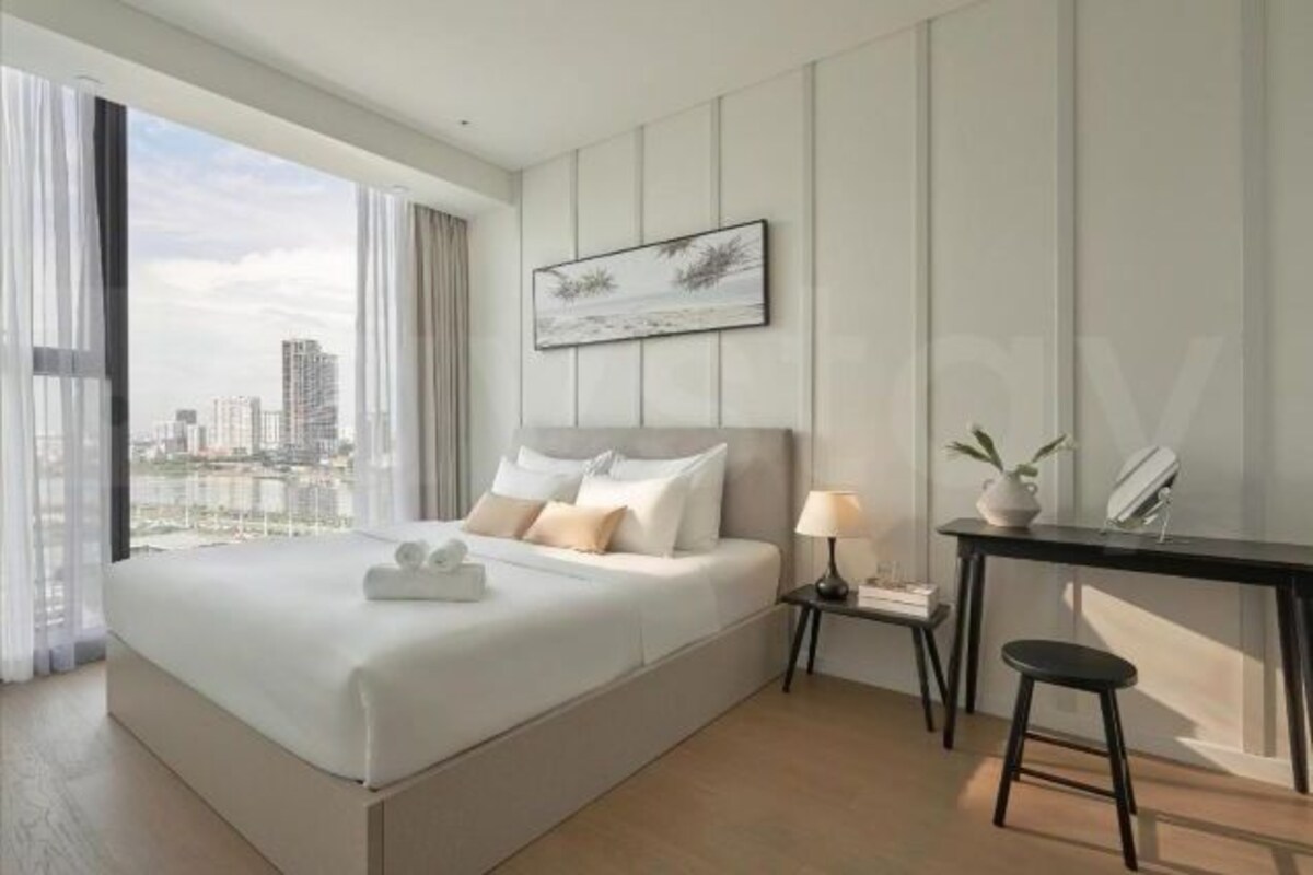 A modern hotel room with a large bed, a desk, a chair, a nightstand, a lamp, and a framed picture on the wall.
