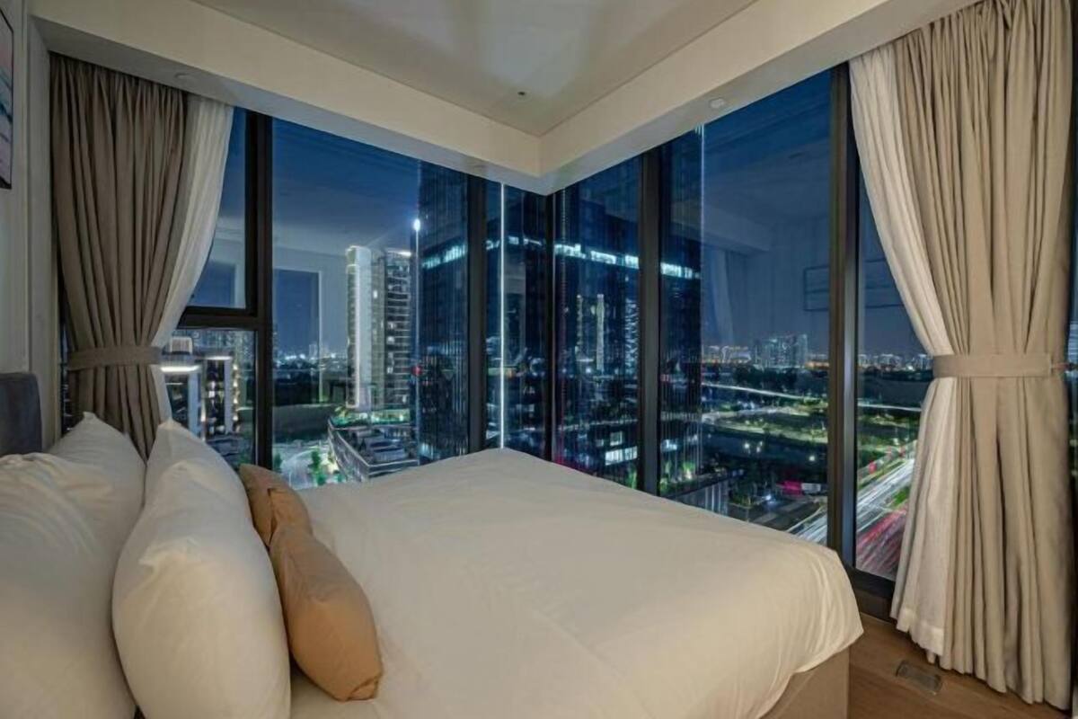 A modern hotel room with a large bed, city view, and large windows.