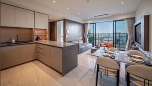 A modern kitchen with a central island, a dining area with a table and chairs, and a large window offering a city view. - The Metropole Riverside Apartment (Ho Chi Minh City)