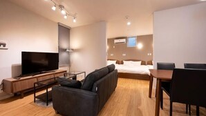 Ein modernes Hotelzimmer mit Sofa, Fernseher, Bett, Schreibtisch und Esstisch.