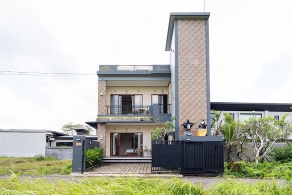A modern two-story house with a balcony, a gated entrance, and a small garden area. - MangBo House by The Lavana (Bali)
