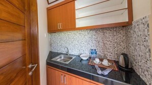 A compact kitchen with a granite countertop, a sink, wooden cabinets, and a backsplash with a speckled pattern. - MangBo House by The Lavana (Bali)