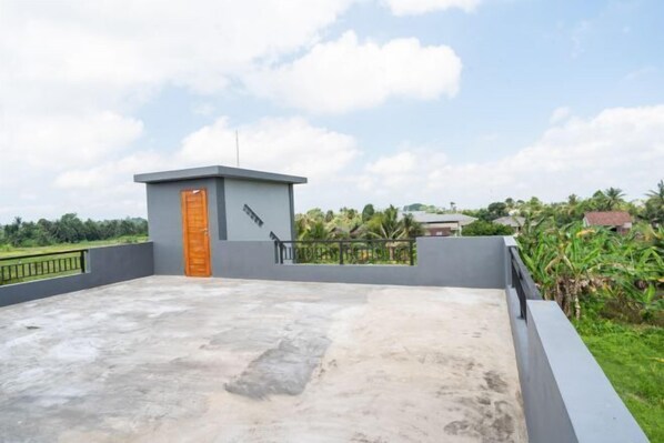 A rooftop terrace with a small structure, a metal railing, and a view of greenery and distant buildings. - MangBo House by The Lavana (Bali)