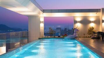 A rooftop infinity pool with a city view, a lounge area, and a poolside table.