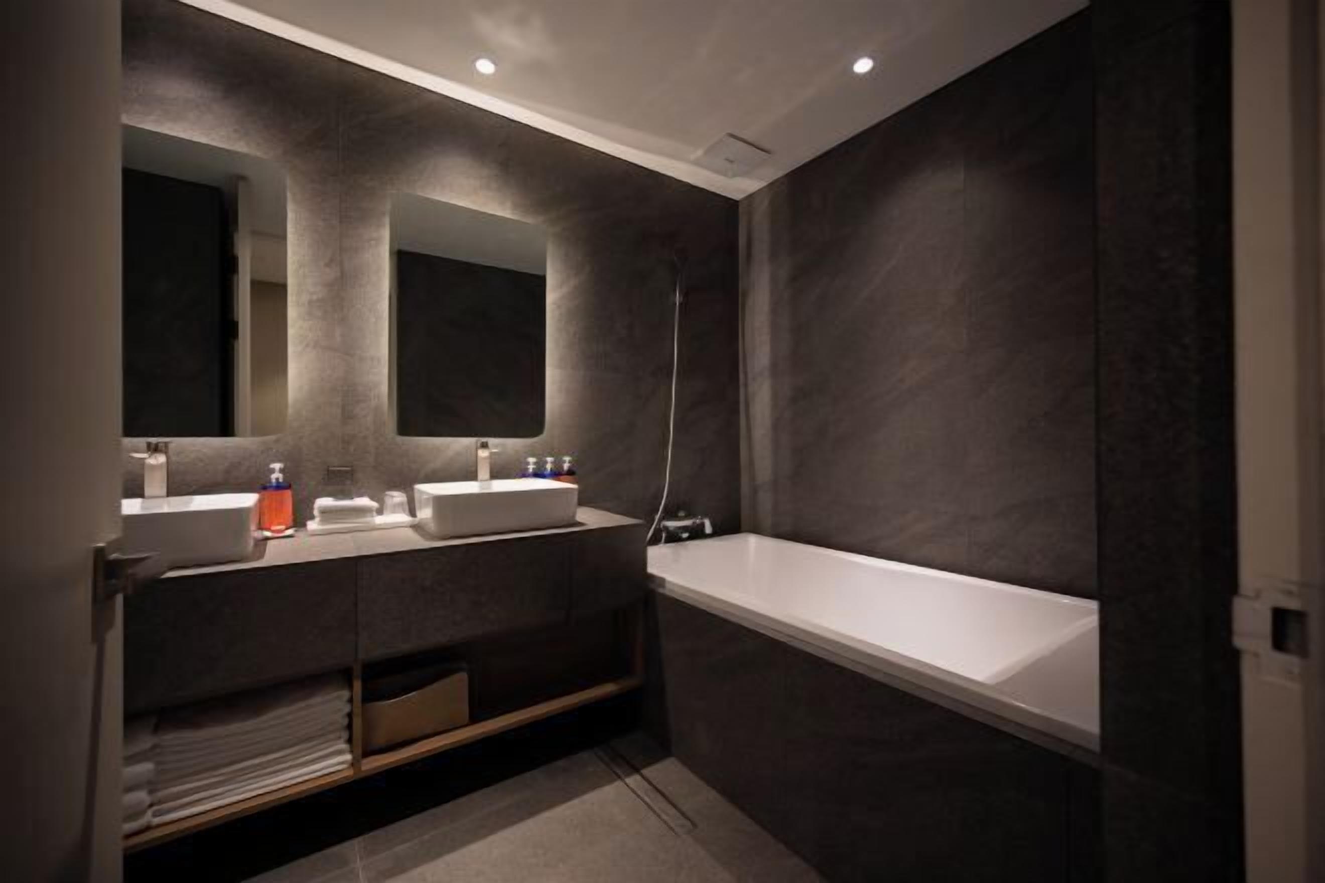 A modern bathroom with dark walls, a white bathtub, and a vanity with two sinks.