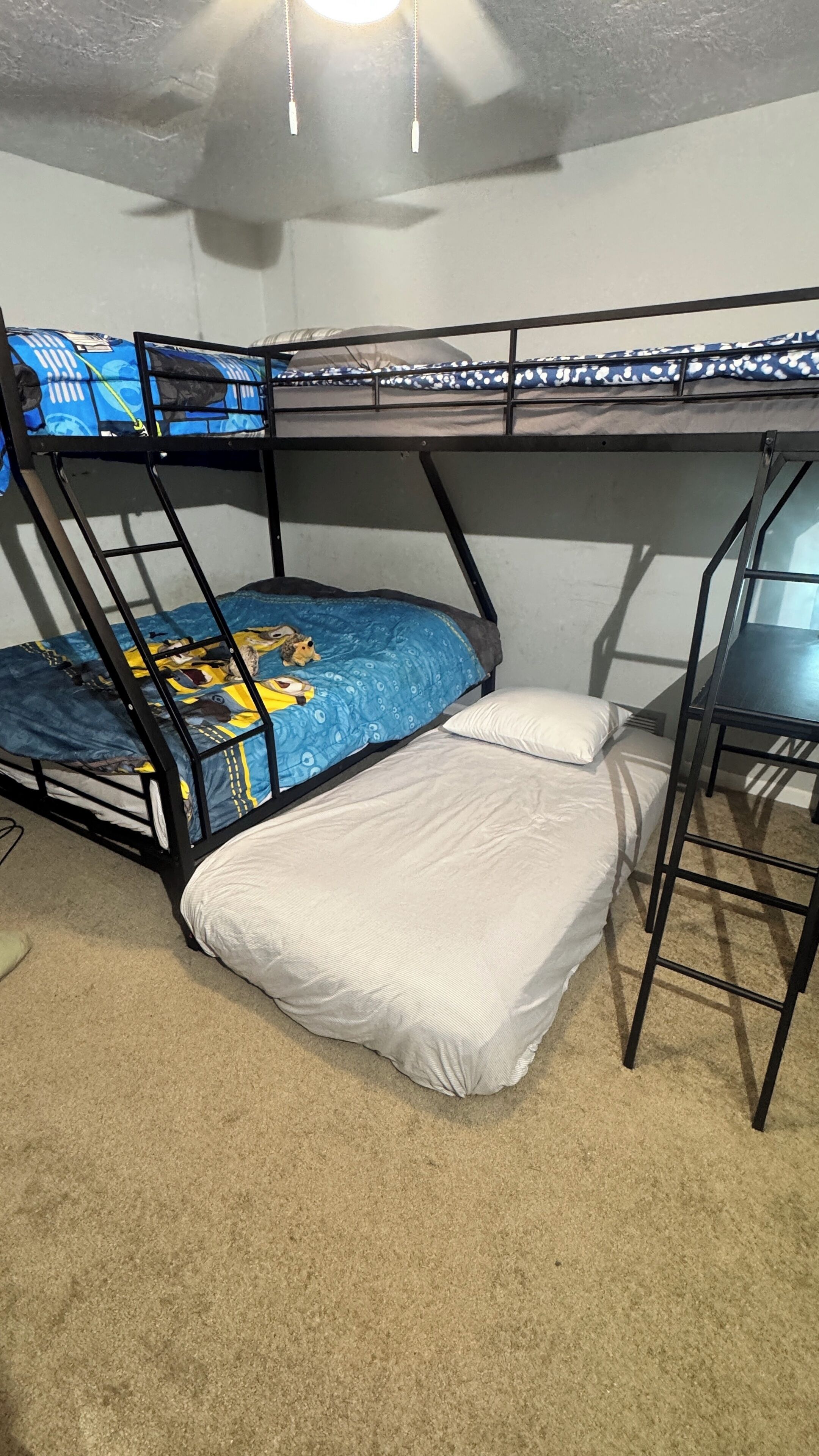 A bunk bed with a blue and yellow bedspread, a white pillow, and a small table beside it.