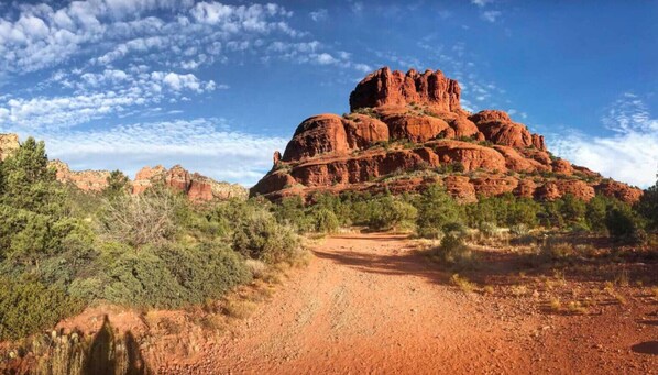 A desert landscape with a prominent red rock formation and a dirt path leading towards it.