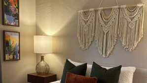 A bedroom with a bed, pillows, a macrame wall hanging, a lamp, and two paintings on the wall. - Relaxing Sedona Condo | Walk to Dining • Bell Rock (Sedona)