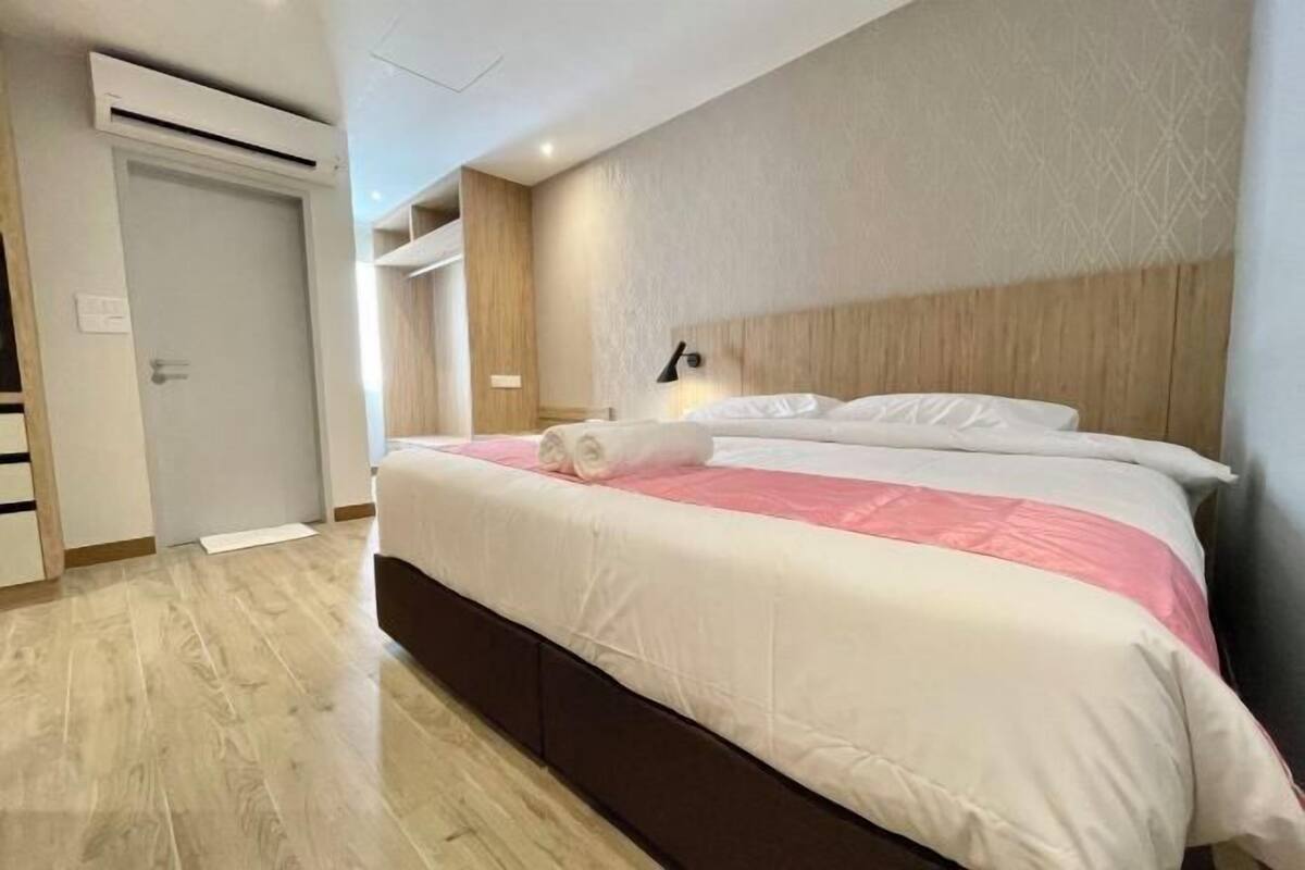 Een hotelkamer met een houten vloer, een bed met wit en roze beddengoed, een bedlampje en een deur met een handgreep.