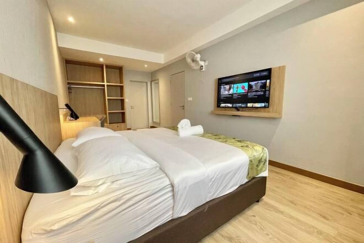 Een hotelkamer met een bed, een aan de muur bevestigde televisie, een bureau met lamp en ingebouwde planken.