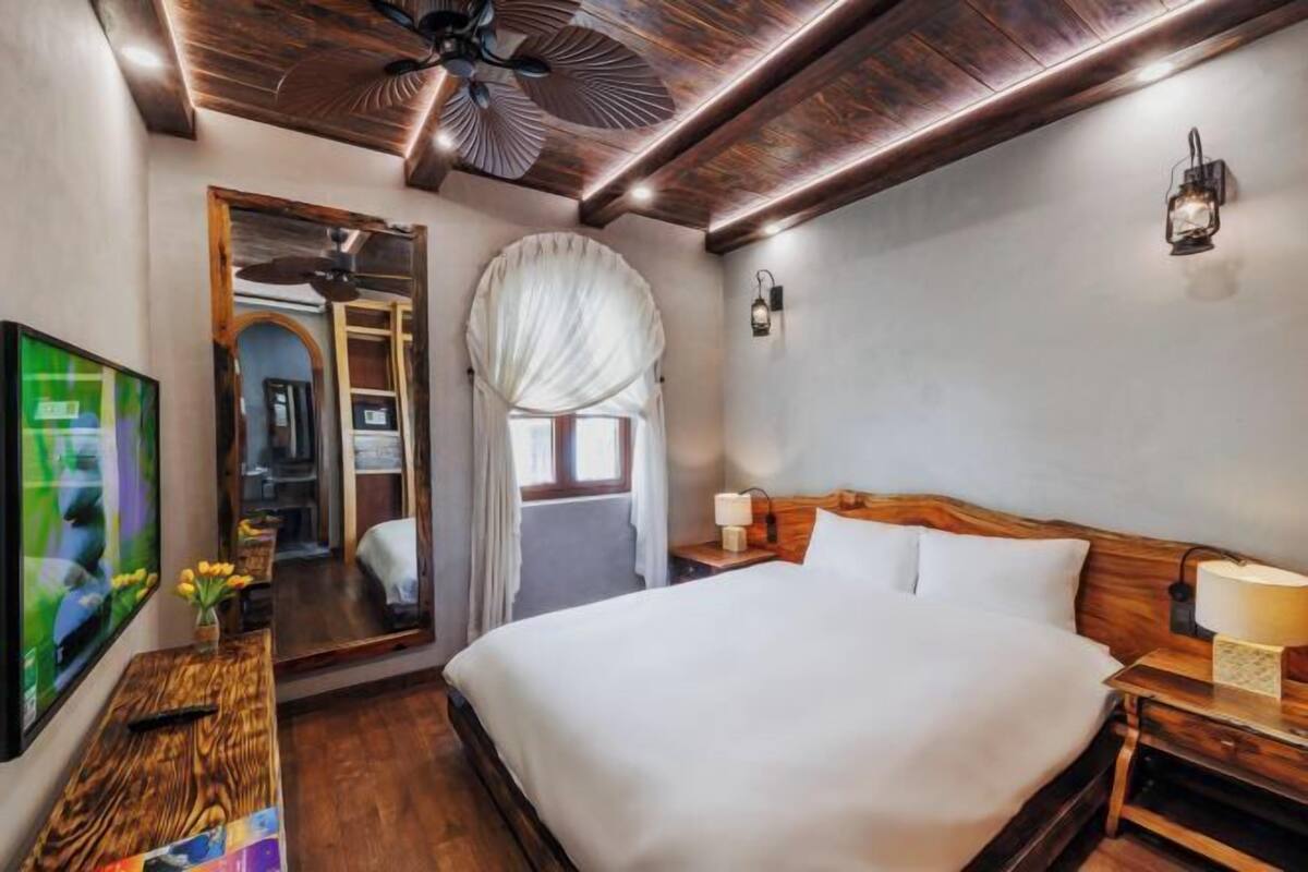 A hotel room with a large bed, wooden headboard, a ceiling fan, a TV, and a mirror.