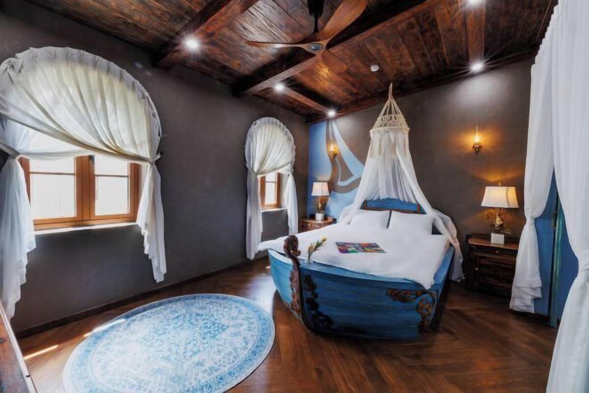 A bedroom with a canopy bed, a round blue rug, and a wooden ceiling.