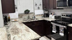 Una cocina con armarios de madera oscura, un microondas de acero inoxidable, un letrero que dice 'cafetería' y un reloj en la pared.
