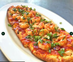 Una pizza de mariscos con camarones y cebollines sobre un plato blanco.